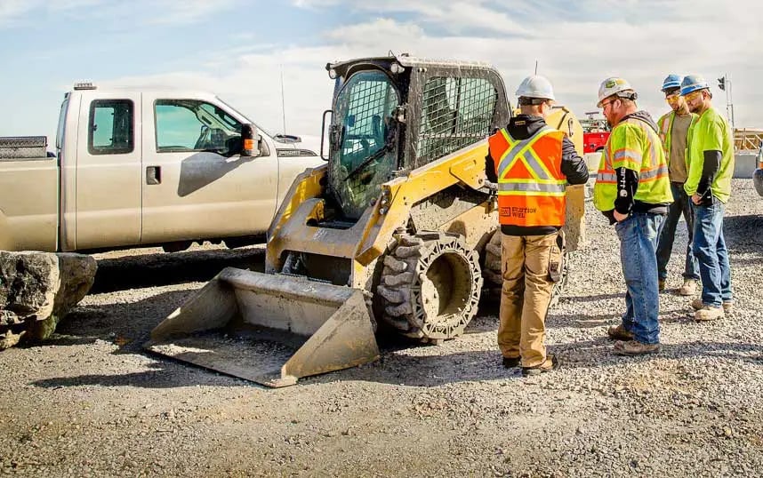 Construction workers looking at the solid skid steer tires on a yellow skid steer