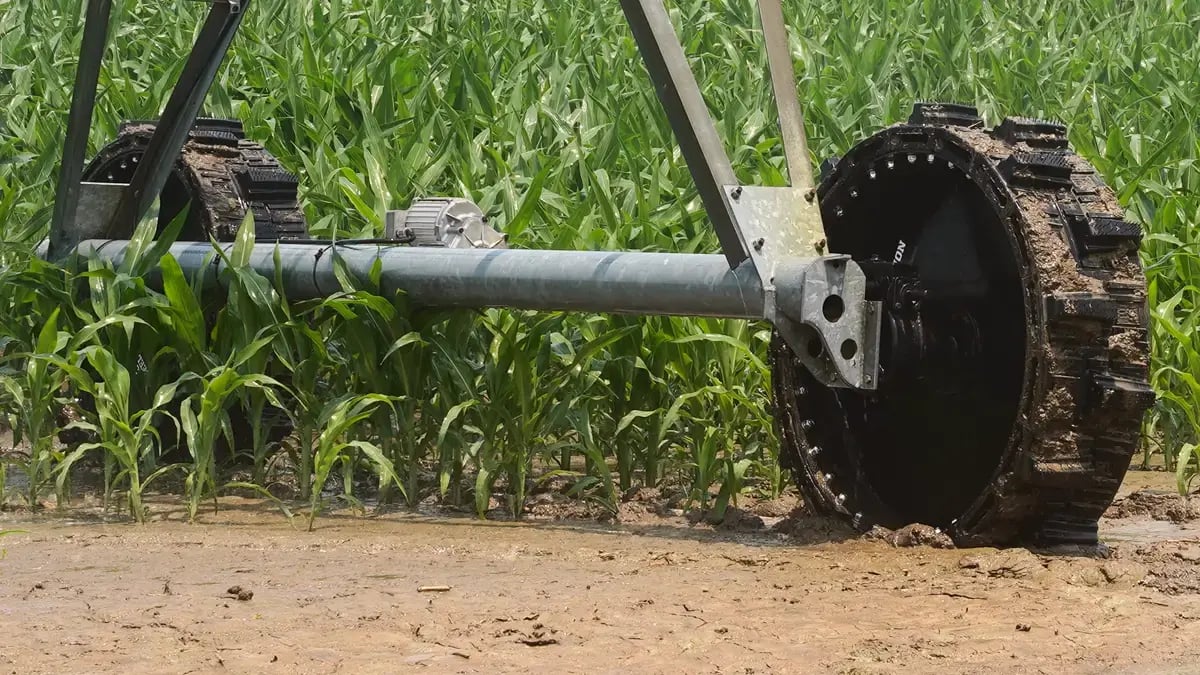 A wide-angle view of a center pivot irrigation system spanning a pasture. Multiple airless EWRS-Pivot-XT tires provide stable, non-flat support across the line. Several brown cattle are grazing freely around the drive units, demonstrating a safe and efficient co-existence