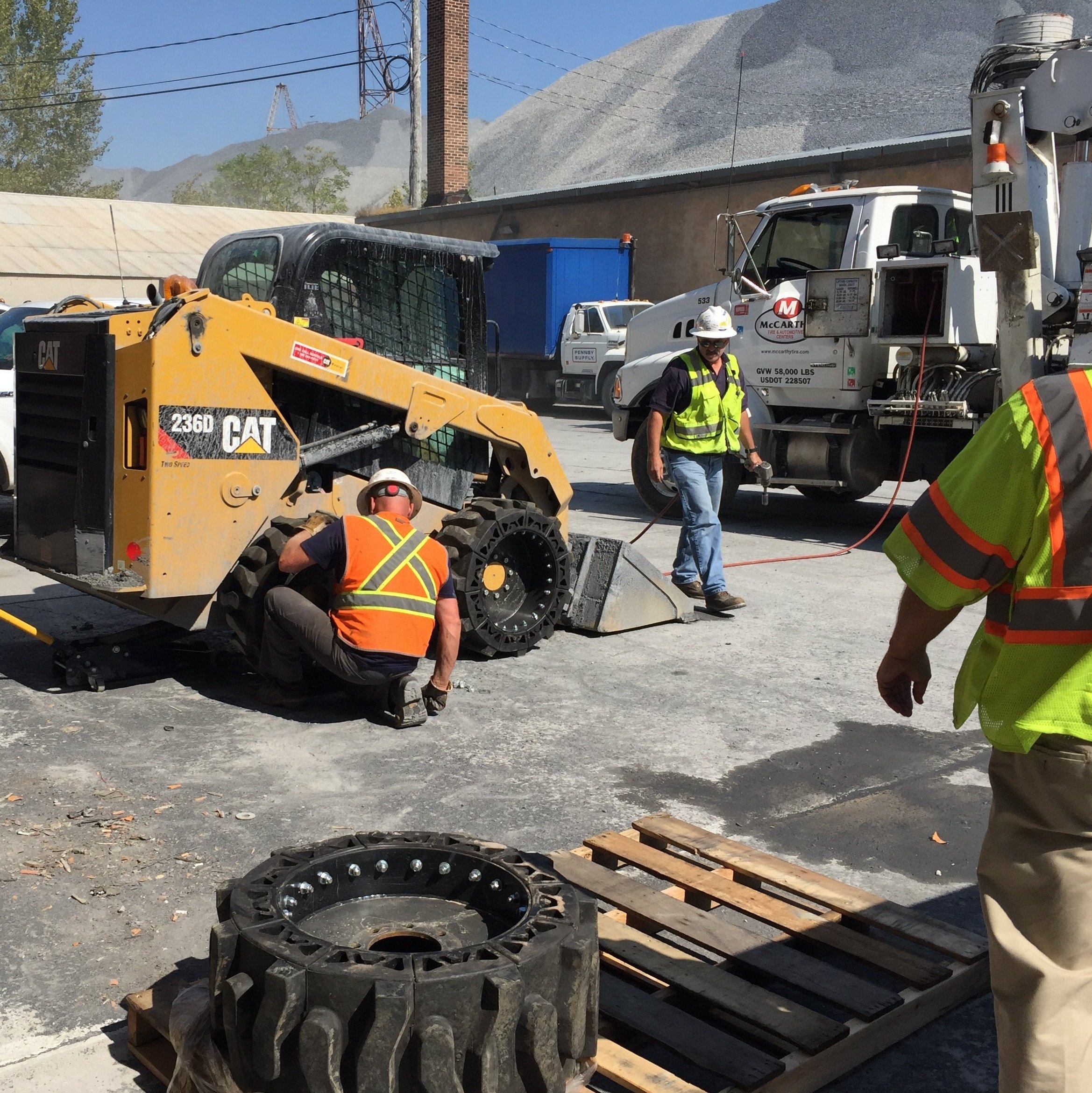 The image shows workers fixing a flat and switching over to our EWRS-AT solid skid steer tires.