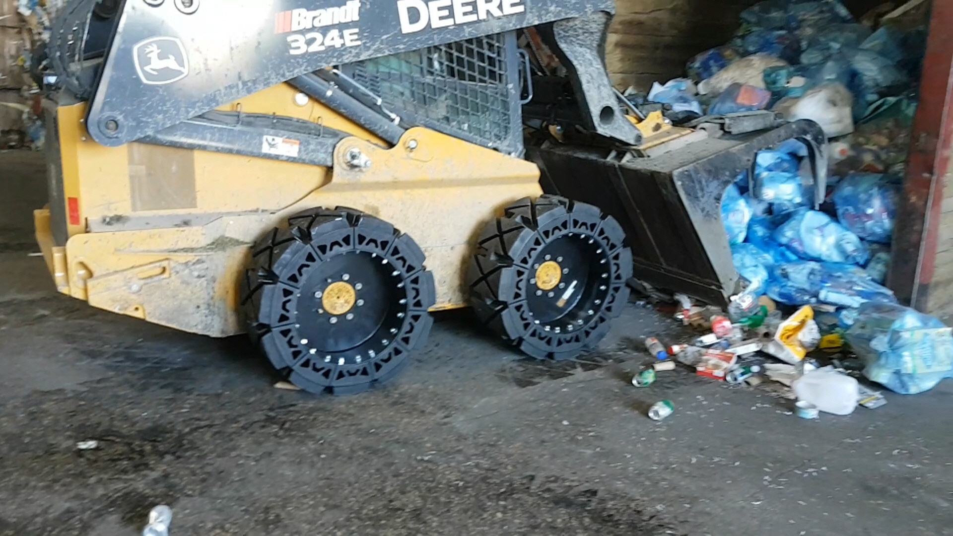 This image shows a yellow skid steer using our EWRS-HS solid skid steer tires in a waste transfer jobsite.